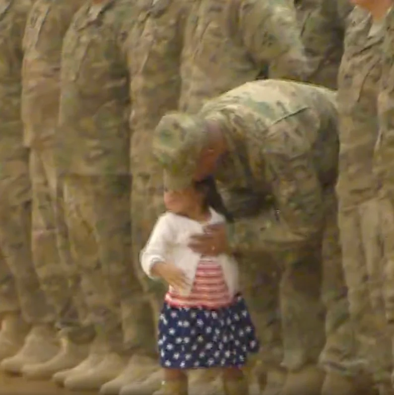 A little girl interrupts the troop's homecoming celebration to give her father a hug